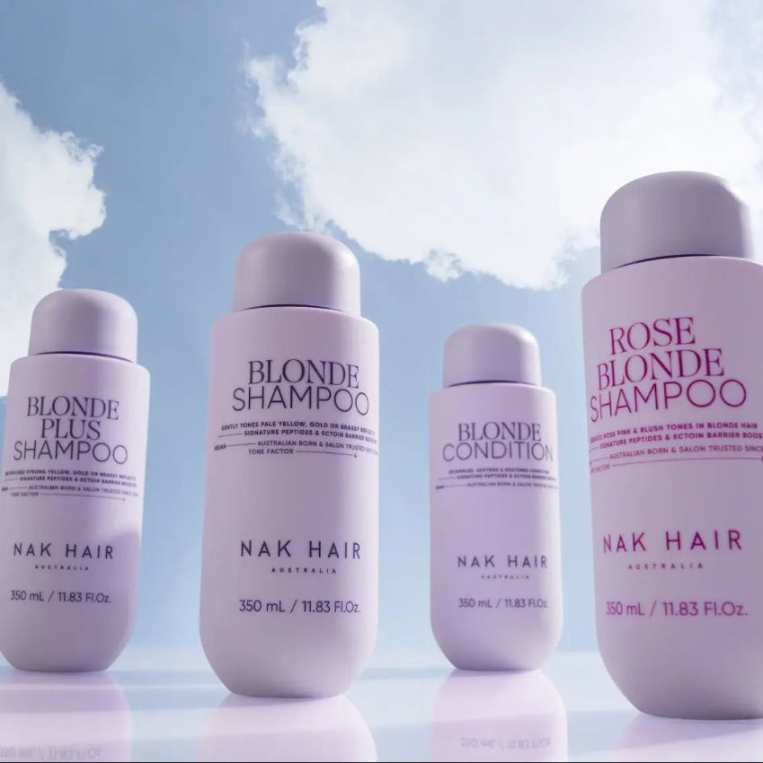 Set of NAK Hair shampoo and conditioner bottles against a light blue sky background