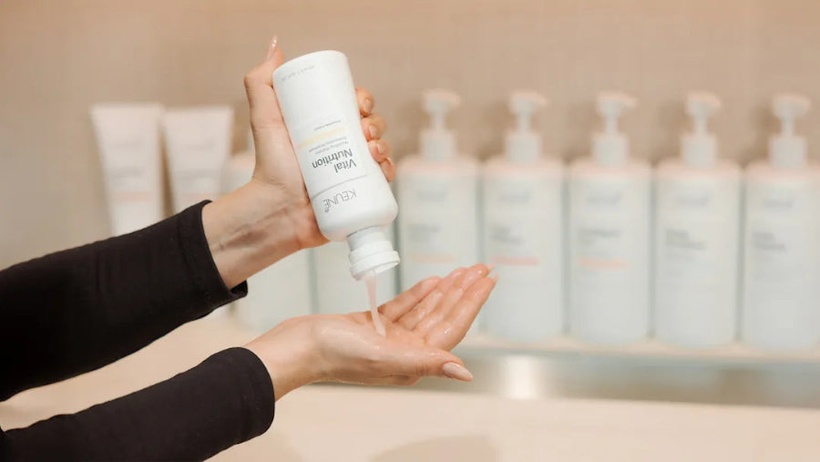 Person holding a white bottle labeled 'Gentle Cleanser' over their palm with a blurred background of similar bottles.